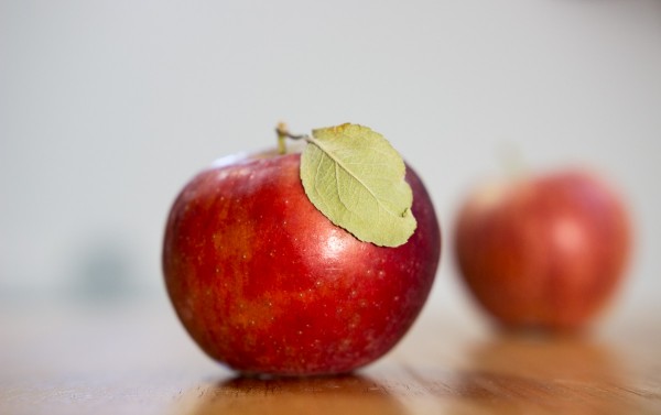 These two apples were photographed with the Sigma 18-35mm F1.8 DC HSM | A lens zoomed to 35mm with an F2.8 aperture for shallow depth of field. Notice how just a sliver of the leaf and near apple is on the focal plane. The front apple is about a foot from the lens, with the farther apple nine inches behind. The back wall with the very soft shadow is ten feet from the camera.  1/40 F2.8 ISO 400, continuous lighting.
