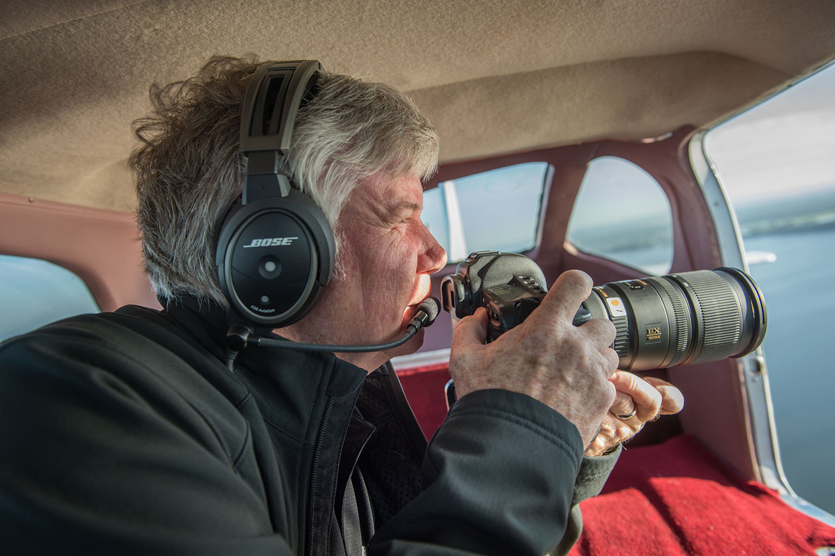 Sigma photographer Jim Koepnick photographing from an open baggage door on a Cessna 210 aircraft.