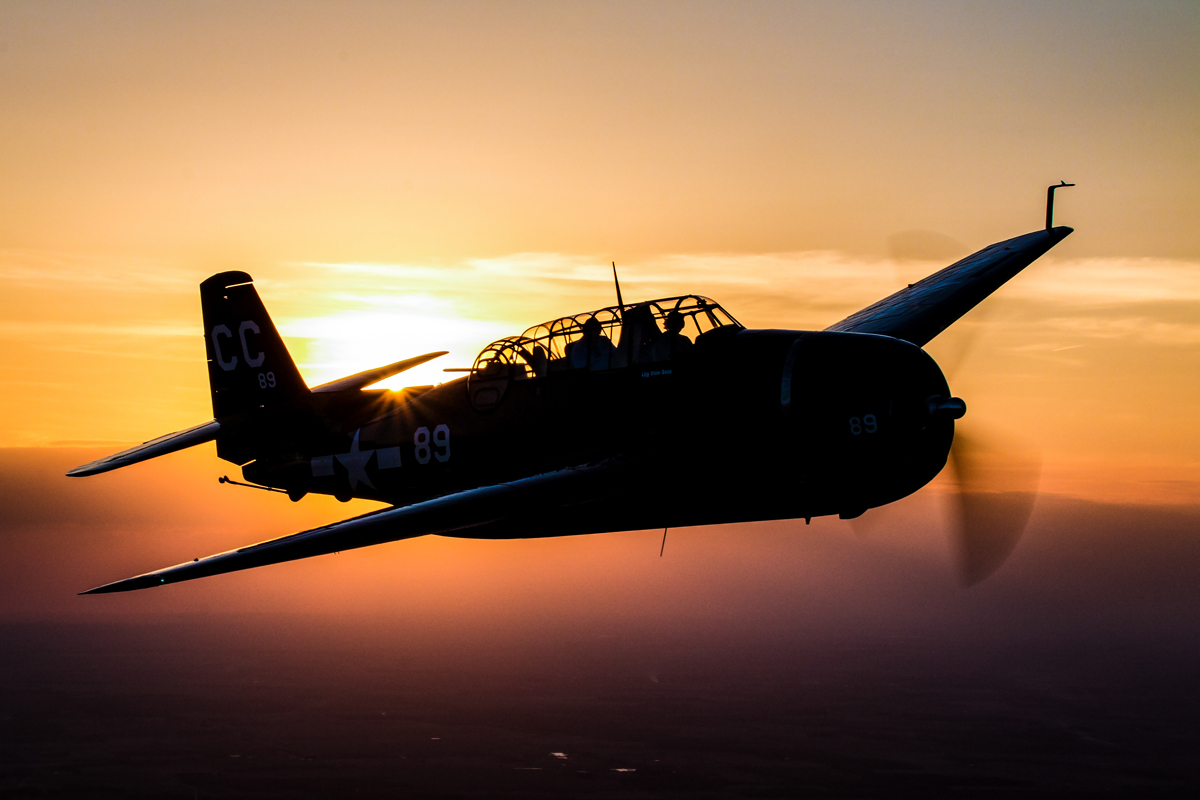 © 2016 Jim Koepnick | Grumman TBF Avenger aircraft silhouetted by the sun. Sigma 18-300mm lens at 1/125 sec at f20 at ISO 200. In a photo such as this, showing the horizon line adds contrast and perspective to the image.