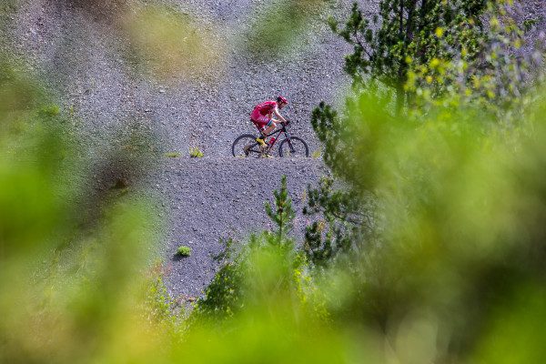 © 2016 Liam Doran | 70-200mm F2.8 DG OS lens on Canon 1DX. ISO 400 f/5.6 at 1/640 sec. I was happy to find this fresh angle on the course. I used the 70-200 and shot through some aspen branches to frame my racer. Red and gren generally work well together and the dark backdrop really makes him pop.