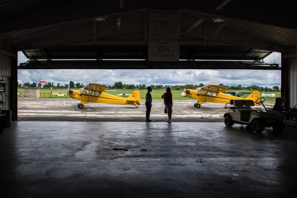© 2016 Jim Koepnick |  A wide shot frames two Piper Cubs with the hangar. Sigma 18-300mm; Nikon D5; 1/2500 sec at f4.5; ISO 400.