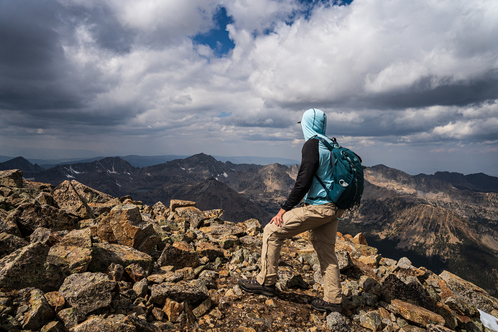 Man in blue and black hoodie, khaki pants, and a blue backpack hiking up a mountain  